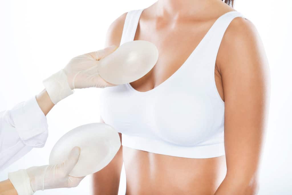 Portrait of female doctor choosing breast implants with her patient over white background.